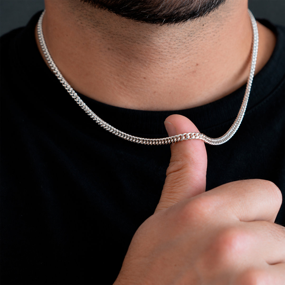 Hombre sosteniendo sobre su dedo una cadena cubana de 4 mm en Plata .925, mostrando el grosor real del tejido Cuban Link y su proporción respecto a la mano.